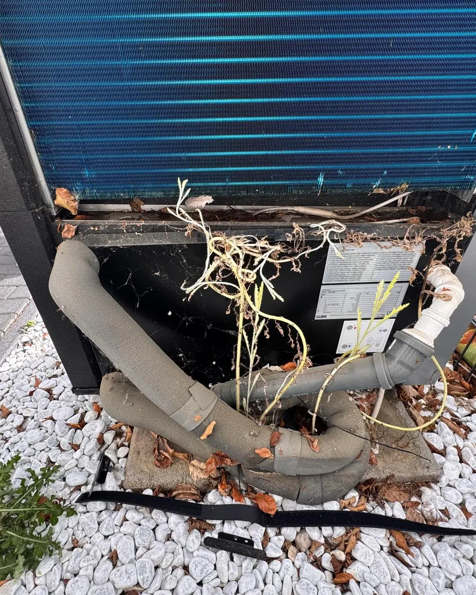 Außengerät einer Wärmepumpe, in das Pflanzen eingewachsen sind, weil das Kiesbett falsch angelegt wurde